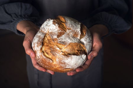 Female hands holding hot homemade baked whole wheat bread.