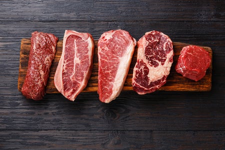 Raw beefsteaks, including strip loin, rib eye, tenderloin and fillet mignon, on a wooden board