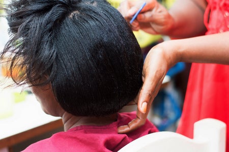 Close-up of a woman's straightened black hair being styled in a salon - showing hands of hairdresser.