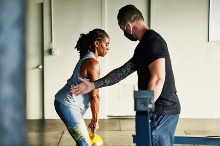 Gym owner helping mature female client with technique during workout in gym