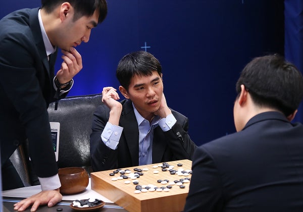 Three men contemplate a Go board.