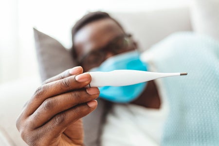 Black man laying on sofa checking fever with thermometer