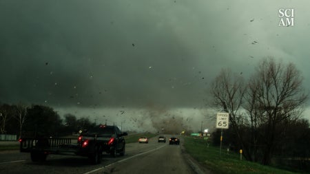 Cars on a highway with a tornado in a few hundred feet in the distance that has thrown debris into the air