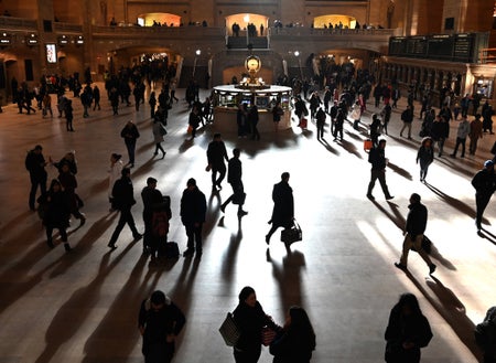 Silhouettes of commuters walking inside a large train station in NYC