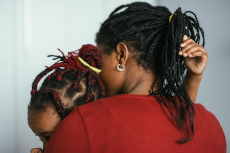 Unrecognizable black mother embraces her daughter in bedroom