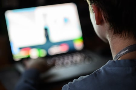 Head of teenager with student band around neck looking at a blurry computer desk.