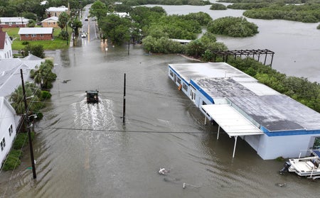 Flooded streets with National Guard vehicle driving towards area with trees.