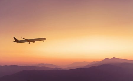 Airplane silhouette in the sky with orange mountains and sky.