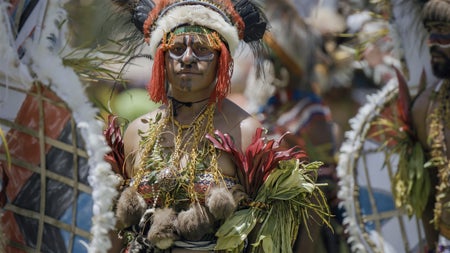 A Papua New Guinean woman in a colorful headdress and outfit surrounded by others in color outfits